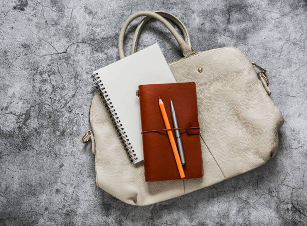 istock Women's business white leather bag with office accessories notepad organizer on a grey background, top view 1208798160
