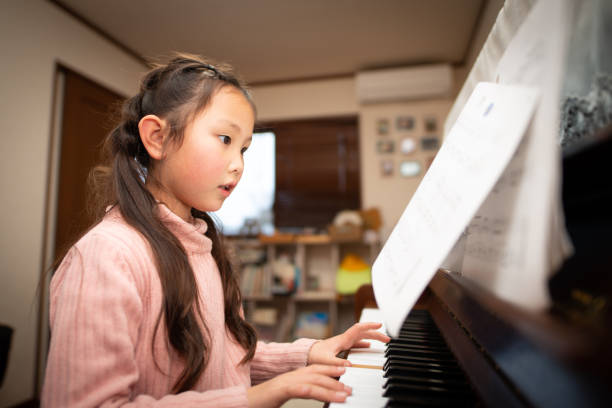 chica practicando el piano mirando partituras de música - looking away asian ethnicity child little girls fotografías e imágenes de stock