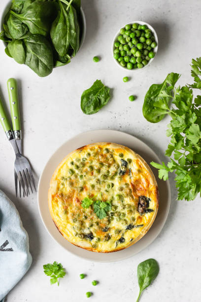 istock Spinach and green pea quiche, tart or pie with ingredients for baking. Light grey background, copy space. 1208804314