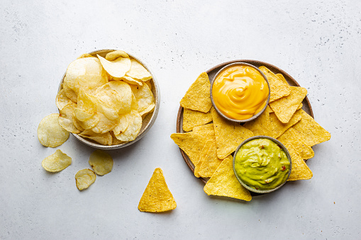 Nachos chips in a bowl with sauces guacamole and cheese, dip variety, over white stone background, top view.