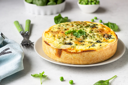 Spinach and green pea quiche, tart or pie with ingredients for baking. Light grey background, copy space.