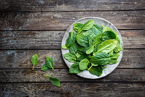 Fresh baby spinach leaves in the plate on old rustic wooden table, organic food, top view.