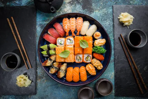 Set of sushi and maki with soy sauce over blue stone background. Top view with copy space