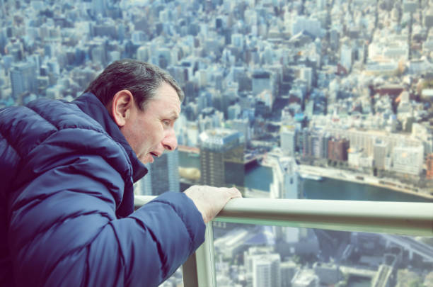 Mature man grunting in fear looking at the panorama of a big city from above stock photo