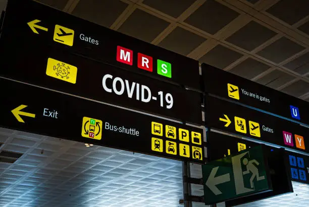 Information panel with Covid-19 word on it at an international airport, symbolizing the global spread of the coronavirus through global air traffic