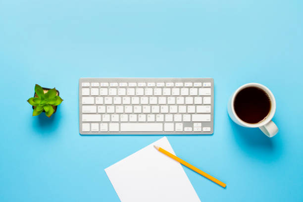 istock Keyboard, flower and cup with tea or coffee, a blank sheet and a pencil on a blue background. Concept workspace, work at the computer, freelance, office. Banner. Flat lay, top view 1208830104