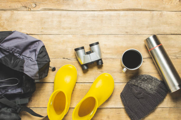 istock Yellow rain boots, backpack, binoculars, camping equipment on a wooden background. The concept of hiking, tourism, camp, mountains, forest. Banner. Flat lay, top view 1208830834