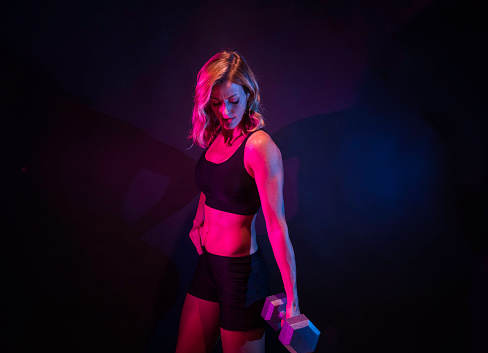 Side view of aged 20-29 years old who is beautiful caucasian female exercising in front of colored background wearing sports bra who is happy and being active with cross training