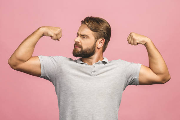 retrato de cintura arriba de joven musculoso flexionando sus bíceps contra fondo rosa. - waistup fotografías e imágenes de stock