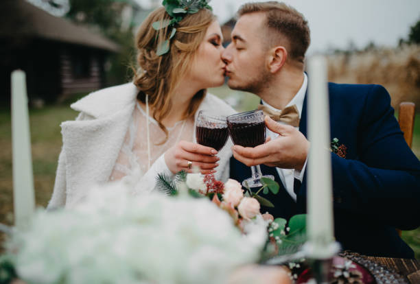 recém-casados sentam-se perto da mesa de banquete, beijão de vinho e beijo. - wedding couple toast glasses - fotografias e filmes do acervo