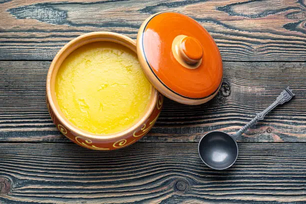 Photo of Pure OR Desi Ghee also known as clarified liquid butter. Pure OR Desi Ghee in ceramic bowls on an old wooden table.