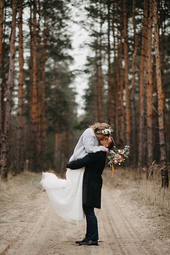 Newlyweds have a fun and embrace at forest path in a coniferous forest among pine trees.