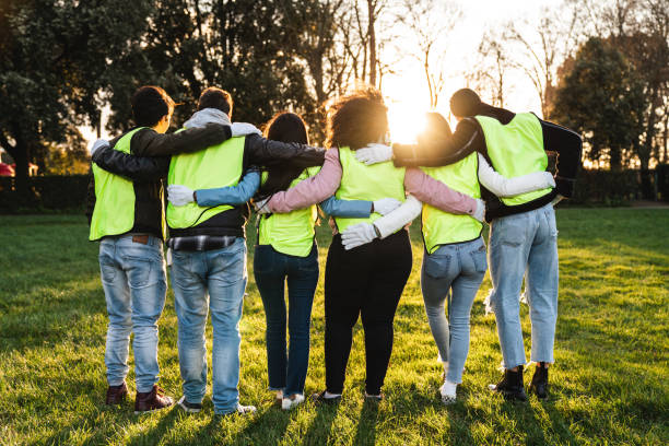 Rear view of teenager volunteers embracing together Rear view of teenager volunteers embracing together. They are wearing bibs. Multi ethnic group. altruism photos stock pictures, royalty-free photos & images