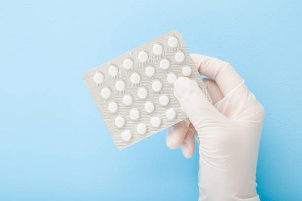 doctor hand in white rubber protective glove holding blister pack of pills. light blue background. pastel color. medical and pharmacy concept. closeup. top down view. - blister pack pill medicine healthcare and medicine imagens e fotografias de stock