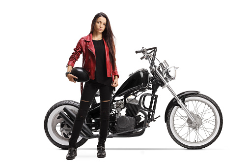 Full length portrait of a young woman holding a helmet and standing next to a custom motorcycle isolated on white background