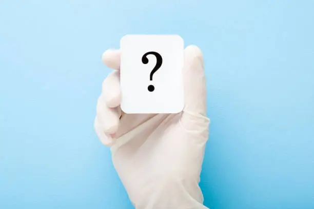 Photo of Doctor hand in white rubber protective glove showing question mark. Light blue background. Concept of medical issues. Closeup. Top down view.