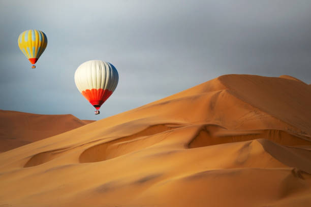 istock Colored hot air balloons flying over the sand dunes at sunset 1208844568
