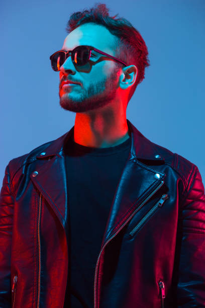 Young talented musician. Caucasian man's portrait isolated on blue studio background in neon light. Beautiful male model in leather wear. Concept of human emotions, facial expression, sales, ad.