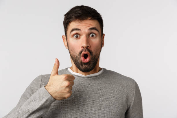 istock Surprised and fascinated, amazed speechless bearded guy in grey sweater react to wonderful amusing event, show thumb-up in like, approval or accepting gesture, gasping say wow, white background 1208847903