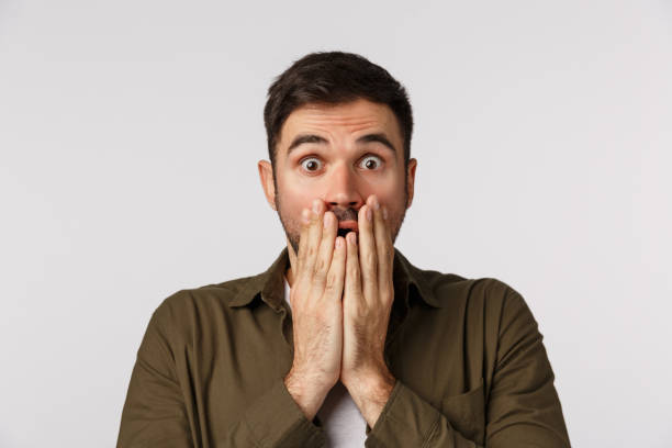 istock No way, awesome. Impressed charismatic, handsome bearded guy in coat, close mouth with palms pressed lips, stare camera astonished, raise eyebrows in surprise, gossiping, white background 1208848105
