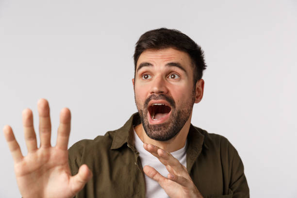 istock Scared and anxious bearded guy screaming as something falling on him, raising hands to defend himself, staring upper left corner bending in danger situation, standing frightened white background 1208848175
