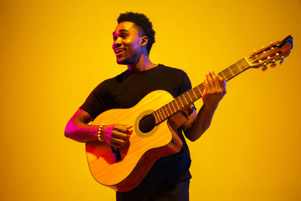 istock Young african-american musician singing, playing guitar in neon light 1208849016