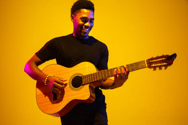 istock Young african-american musician singing, playing guitar in neon light 1208849041