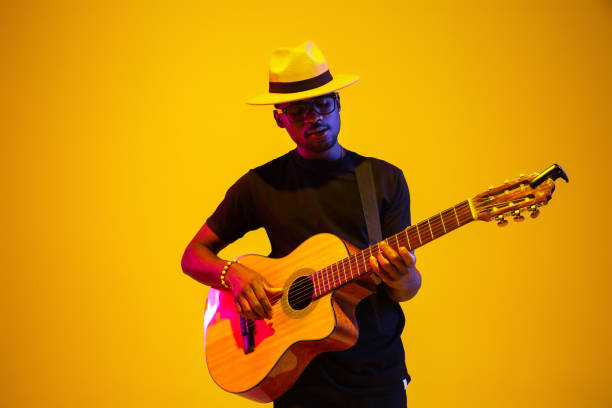 Young african-american musician singing, playing guitar in neon light