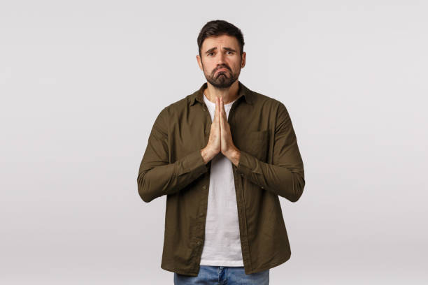 istock Sad, gloomy and miserable, depressed young man need help, begging for forgiveness, apologizing, press palms together in pray, supplicationg, frowning and pulling grimace, white background 1208849301