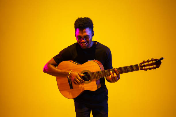 istock Young african-american musician singing, playing guitar in neon light 1208849598