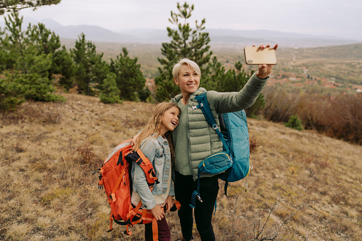 Photo of a young single mother hiking together with her daughter; they are taking a selfie to remember the moment forever