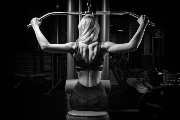 istock Charming blonde does exercises for the back in the gym. Neck pull for the head. The concept of sports, bodybuilding, fitness. Back view. 1208853621