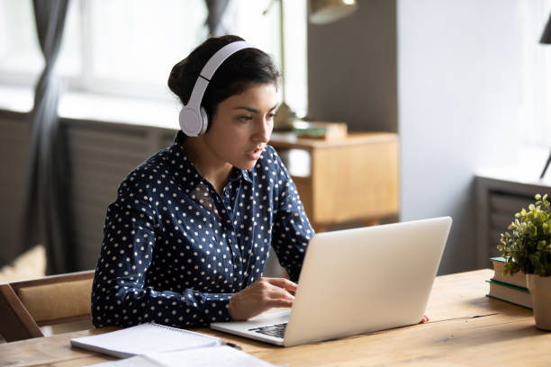 focused indian female in headphones watch webinar on laptop - indian ethnicity audio imagens e fotografias de stock