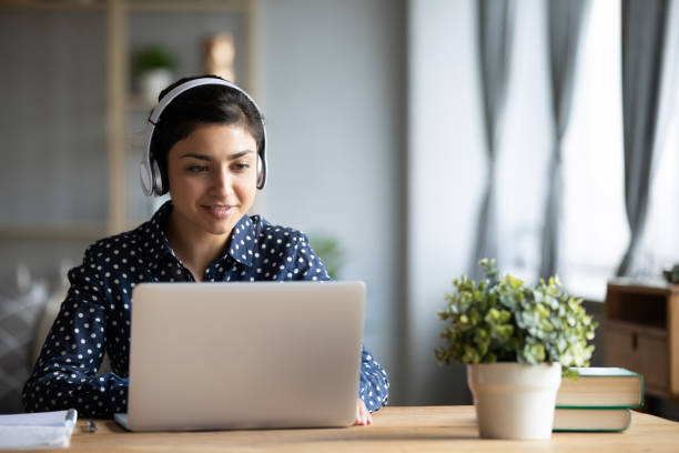 Millennial Indian girl in headphones using laptop at home Millennial Indian girl in wireless headphones sit at desk at home working on modern laptop, young ethnic woman in earphones browsing Internet shopping online or studying on computer in living room audio equipment photos stock pictures, royalty-free photos & images