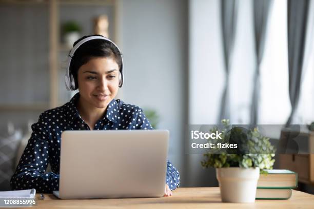 Millennial Indian Girl In Headphones Using Laptop At Home Stock Photo - Download Image Now