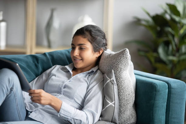 istock Happy indian girl relax on sofa using modern tablet 1208856082