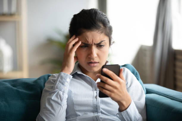 Frustrated girl feel stressed with cellphone problems Confused millennial Indian girl sit at home look at cellphone having operational problems, frustrated young woman feel stressed with slow Internet connection, virus attack or spam on smartphone e mail spam photos stock pictures, royalty-free photos & images