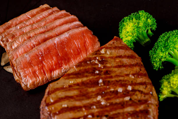 Juicy cooked beef sirloin with broccoli on black background.