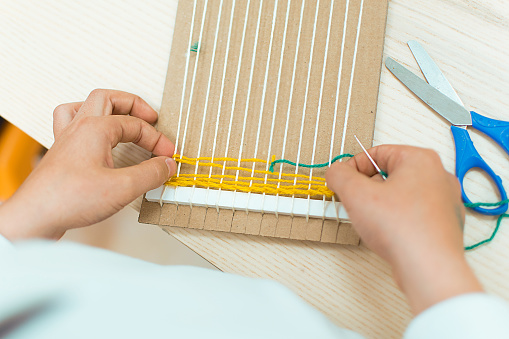 Little children hands weaving loom in art theraphy class at school. Education concept. Telar weave looom