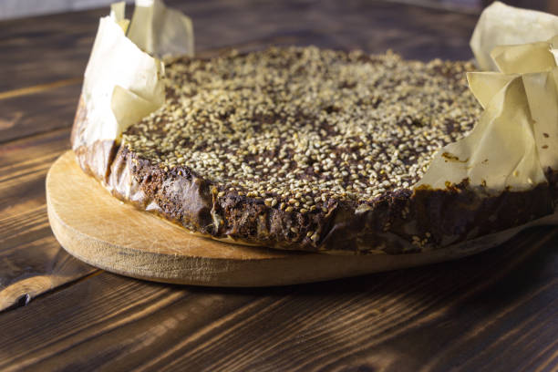 Freshly baked homemade amaranth bread sprinkled with sesame seeds. Hot bread in baking paper, lies on the kitchen board on a wooden table. Only from the oven. Natural healthy food. Selective focus. pan de amaranto casero recién horneado espolvoreado con semillas de sésamo. pan caliente en papel de hornear, se encuentra en la tabla de la cocina sobre una mesa de madera. sólo del horno. alimentos naturales saludables. enfoque selectivo