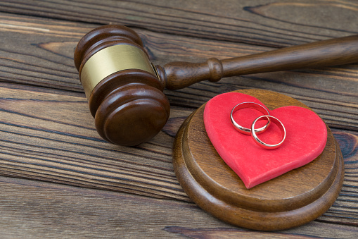 Red heart, wedding rings and judge gavel, on the background of a wooden table. Divorce proceedings concept, court law. Marriage contract