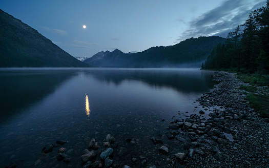 Reflection of the moon in a mysterious foggy lake. Wild russian nature. Beautiful landscape with lake in the mountains. Traveling in the Altai Republic. Active tourism in Russia. Multa Lake.