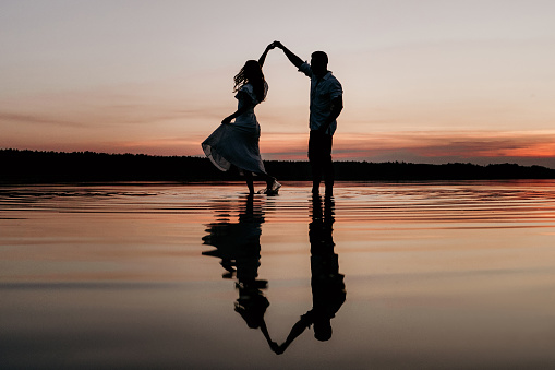 Young couple dancing in the water on Sunset. Two silhouettes against the sun. Romantic love story.