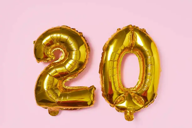 Photo of Golden foil balloon in the shape of numbers 20 on pink background. Cash back or sale concept