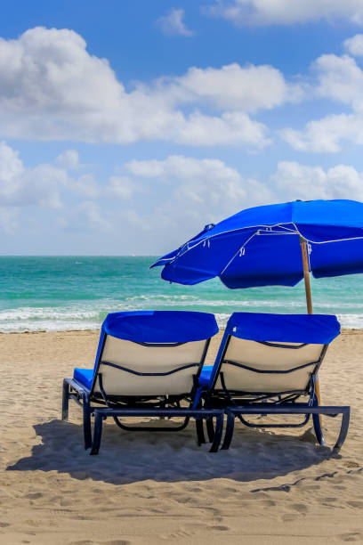 istock Two bright blue beach chairs with matching umbrella sit empty on a deserted beach 1208883484