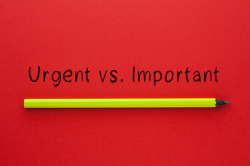 The words urgent vs. important and pencil on red background. Business concept.