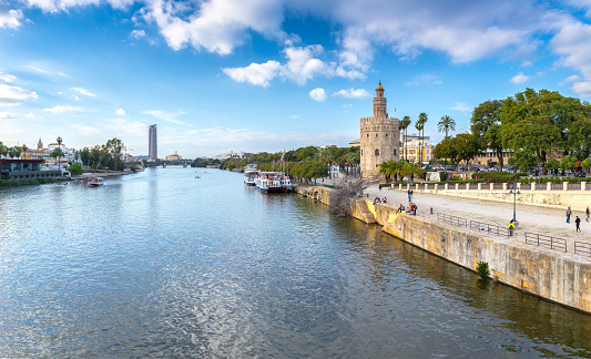 Panoramic view of the waterfront of the Guadalquivir River in Seville, Andalusia, Spain. On a warm winter evening, people relax and stroll along the waterfront.