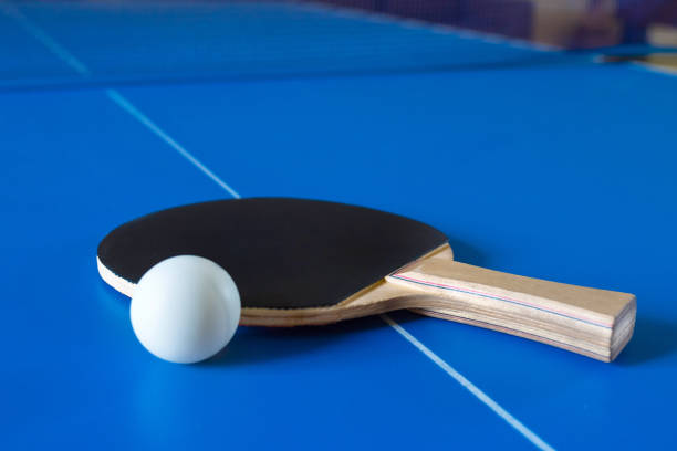 istock Wooden racket for ping pong and white ball lying on the blue table. 1208890471