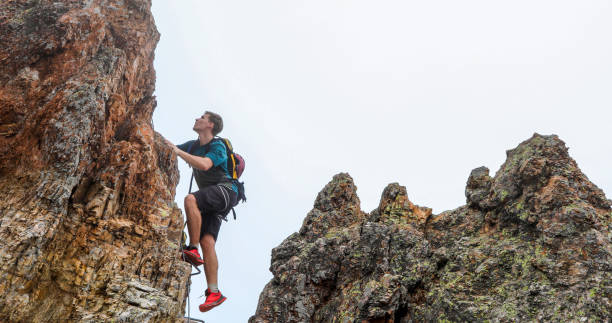 Young man climbs via ferrata ridge in the mist