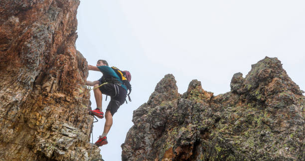 young man climbs via ferrata ridge in the mist - climbing rock climbing rock mountain climbing imagens e fotografias de stock